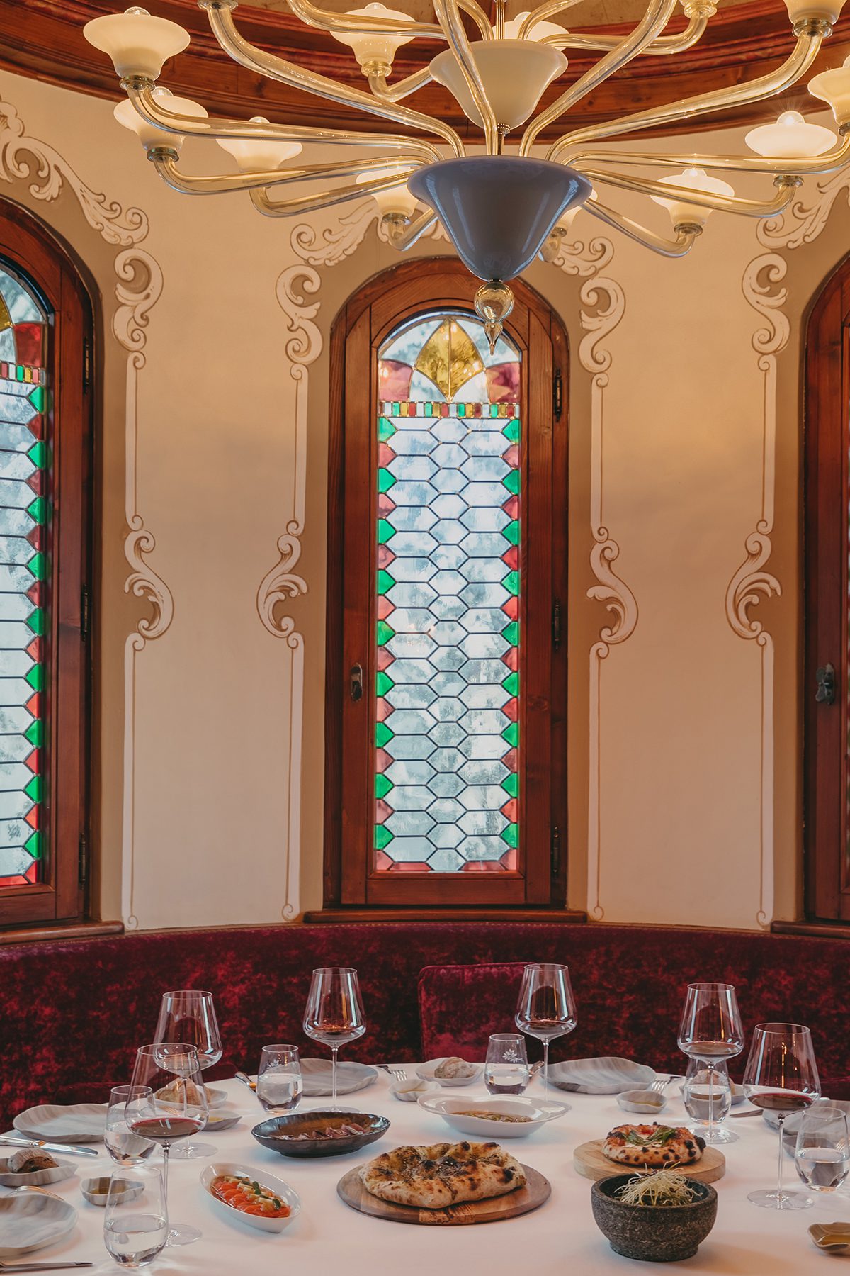 A room with large stained glass windows and red velvet chairs around a table with a white table cloth and wine glasses