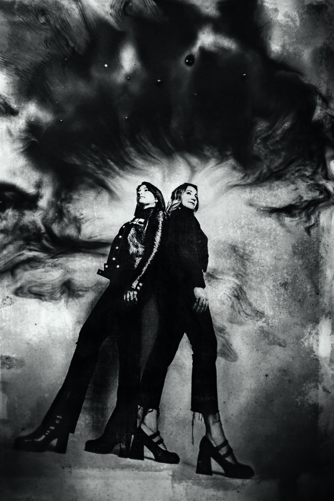 Two girls in black jackets and jeans standing back to back