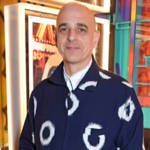 A man wearing pink trousers and a blue and white jumper standing with his hands in his pockets