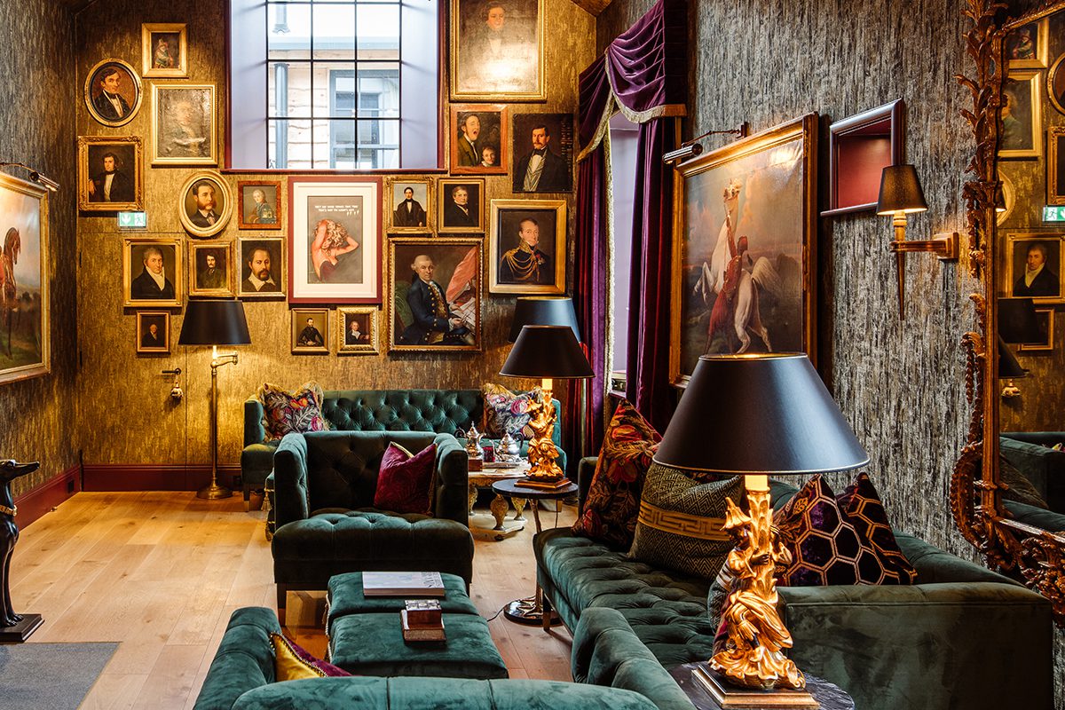 A room with paintings on the walls and green sofas and a gold lamp