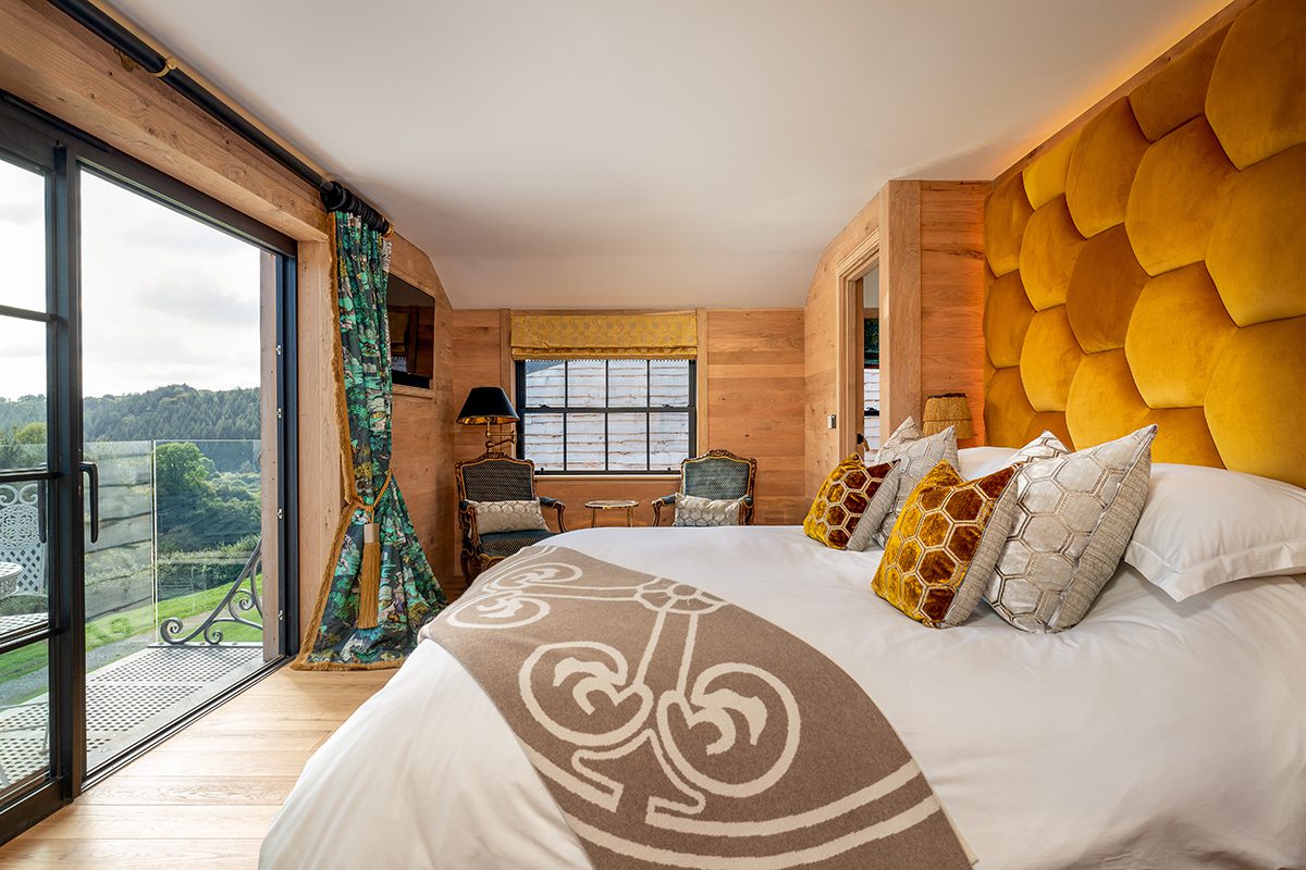 A bed with a yellow headboard and green curtains and a brown throw sprawled across the bed