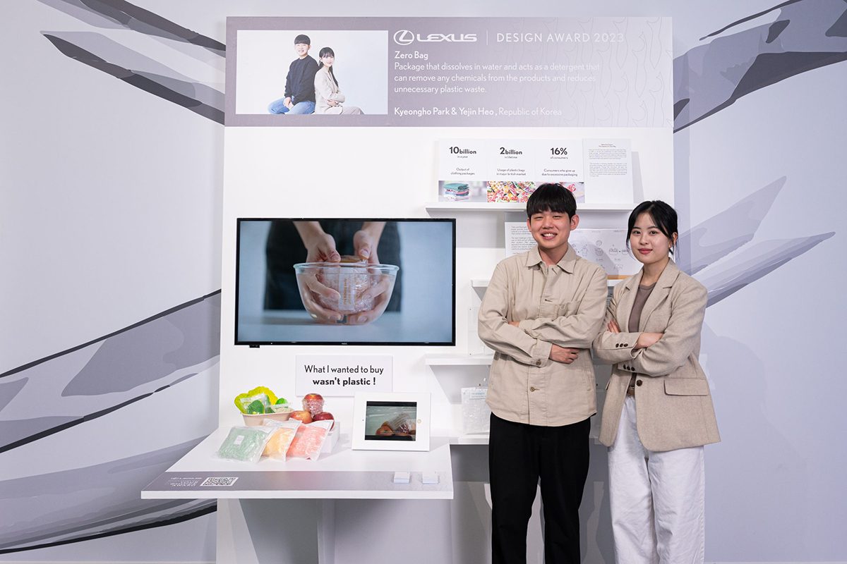 Two men in beige jackets standing next to a screen showing a presentation