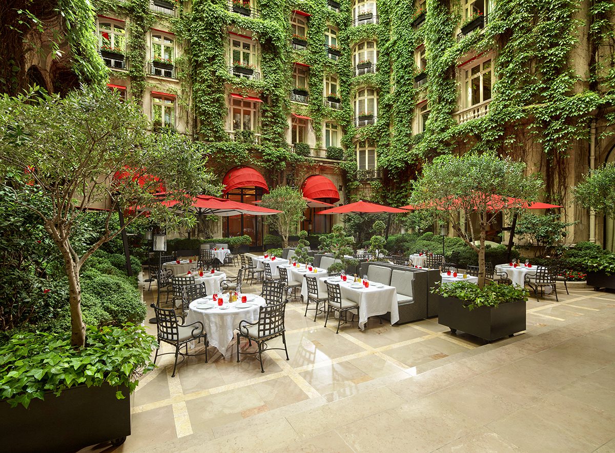 A courtyard with leaves over the windows and red umbrellas