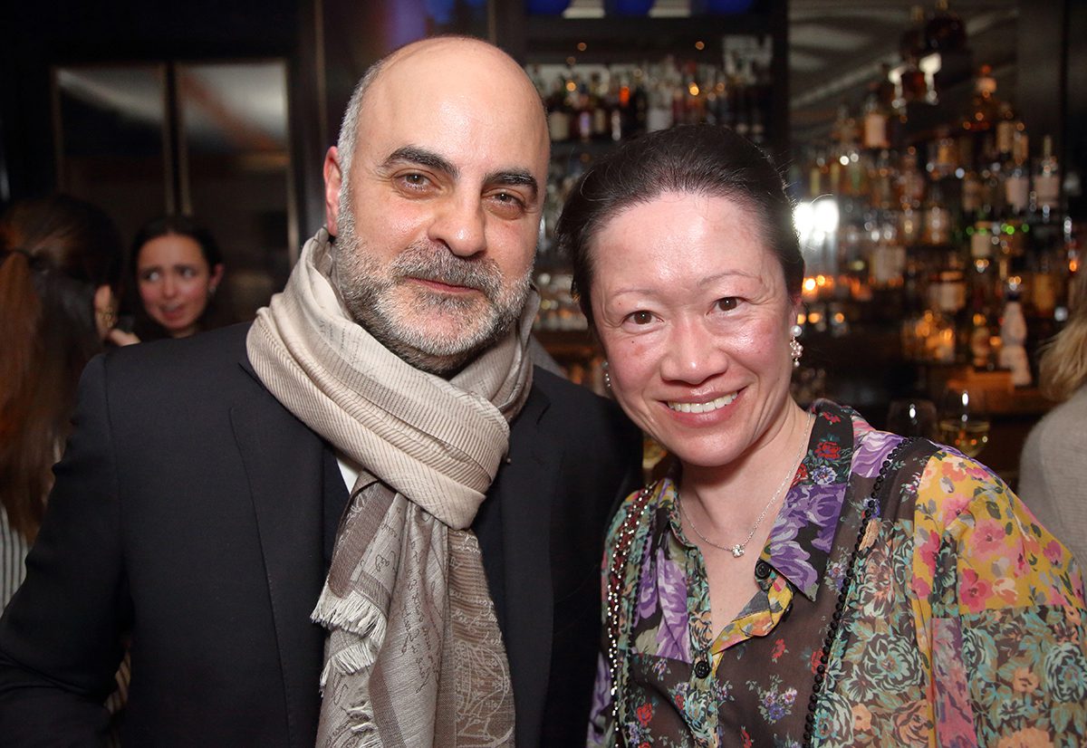 A bald man wearing a scarf standing next to a women with her hair in a bun wearing a purple floral top
