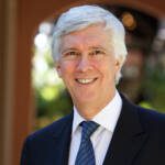 A man with grey hair wearing a suit with a blue tie