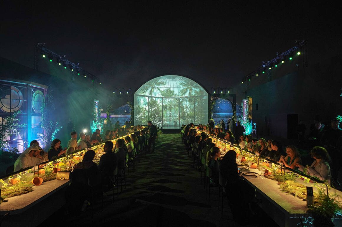 Two long tables in a room with a green light up sign for Richard Mille at the end of the room