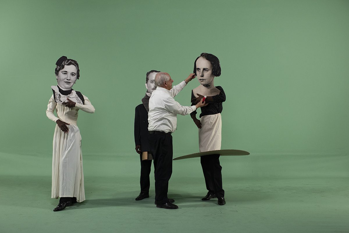 A man fixing a giant head on a costume and another person in a costume watching him