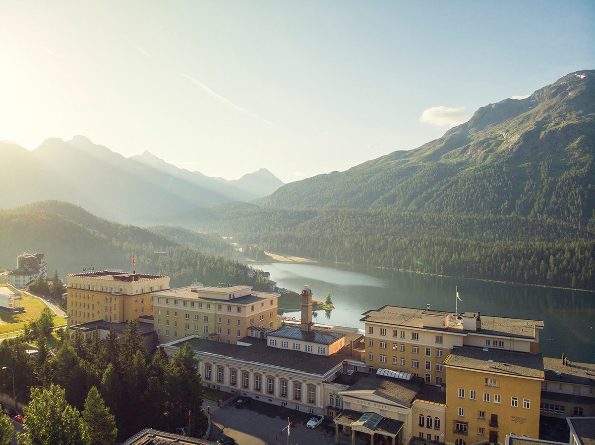 A yellow hotel with a lake and mountains behind it