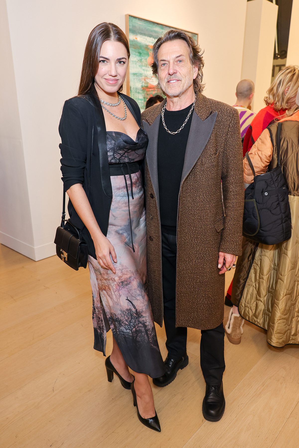 A man in a brown jacket standing next to a women wearing a silk pink and black dress