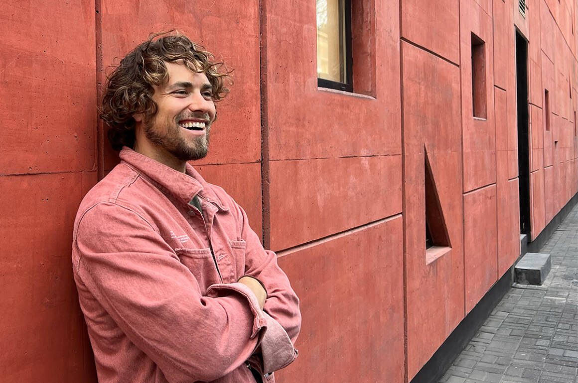 a man wearing a pink jacket standing by a pink wall with his arms folded