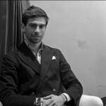 A man sitting down with his hands on this lap wearing a suit