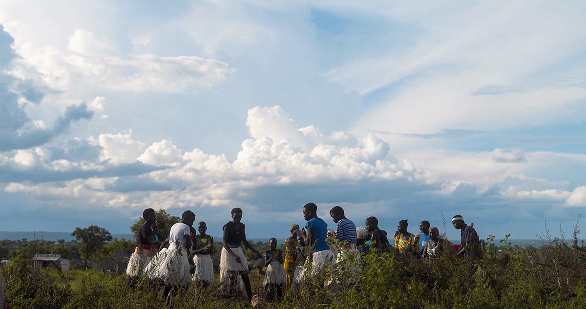 Children dancing outside on the grass with clouds in the sky