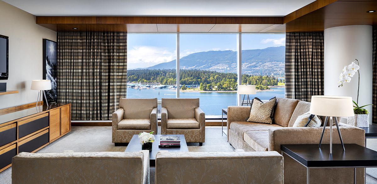 A room with cream chairs and wooden tables overlooking the sea and mountains