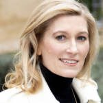 A blonde woman wearing a black turtle neck and a white coat