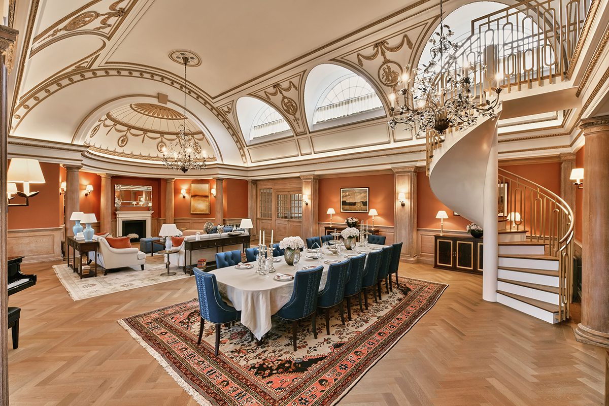 A dining room with blue chairs and arched ceilings and a rug beneath the table