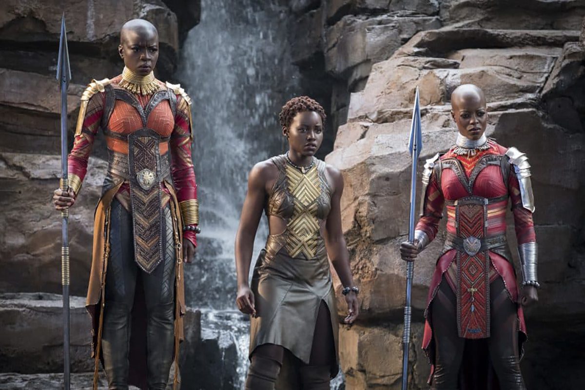 Three people in armour standing with swords by a waterfall