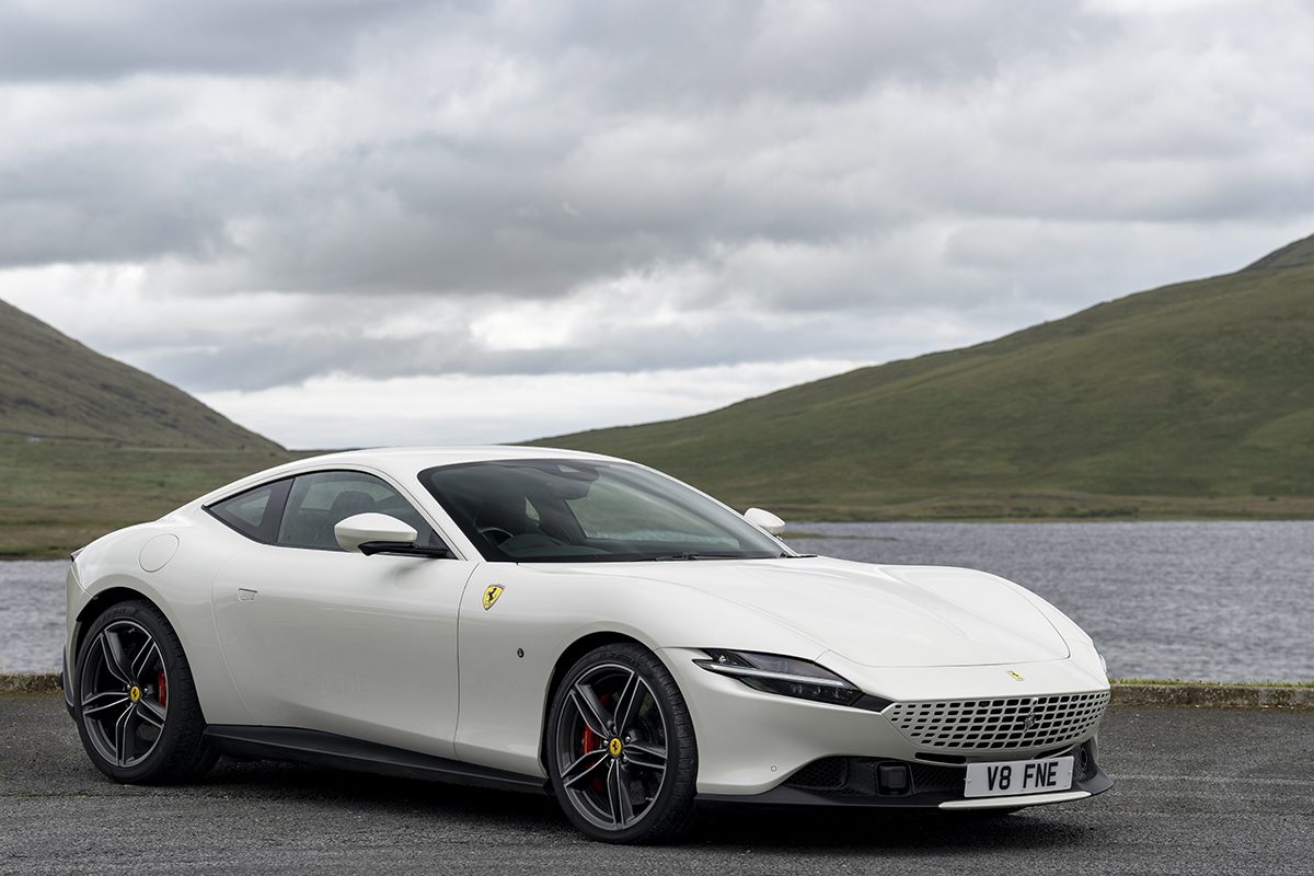 A white Ferrari by a river and hills