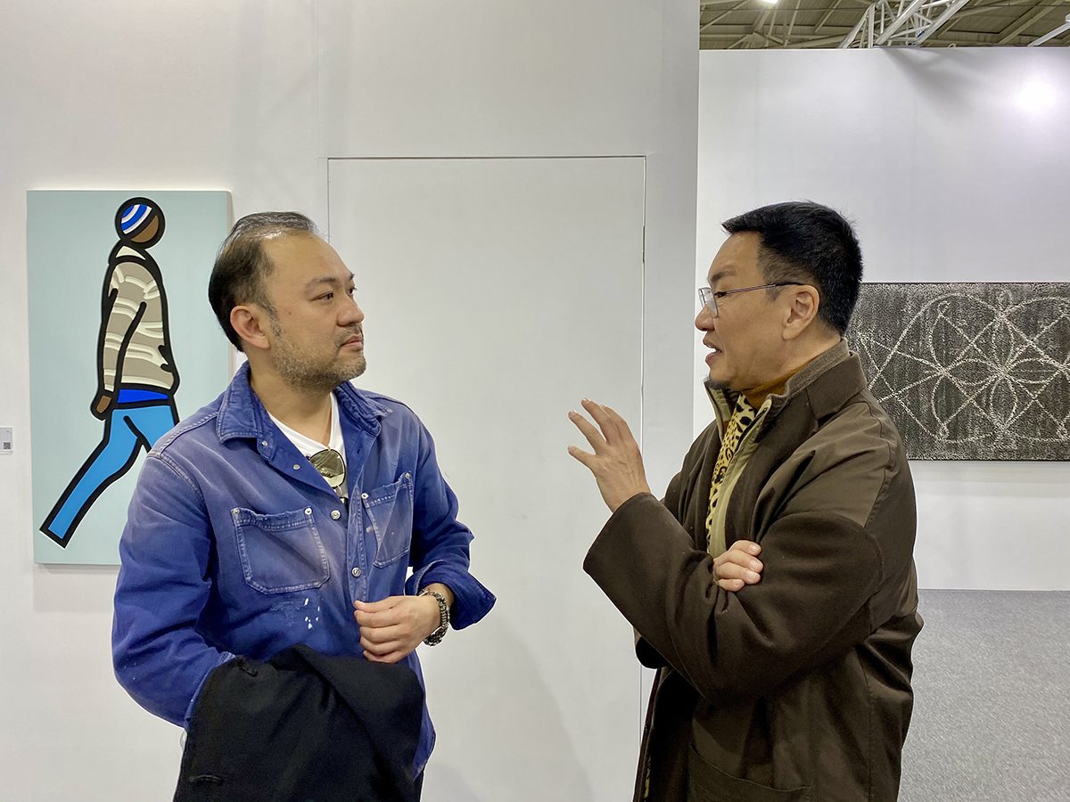A man in a blue jacket speaking to a man in a brown jacket