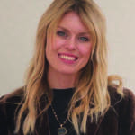 A blonde woman wearing a brown jacket with her hand together
