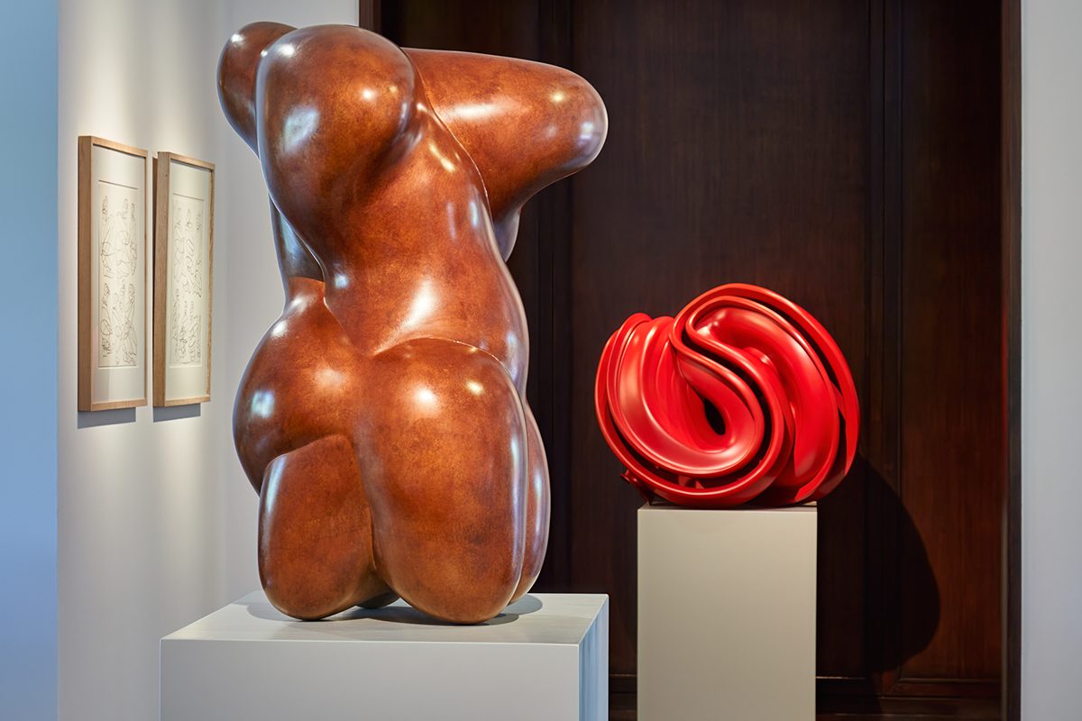 A wooden sculpture and a red sculpture on podiums next to eachother
