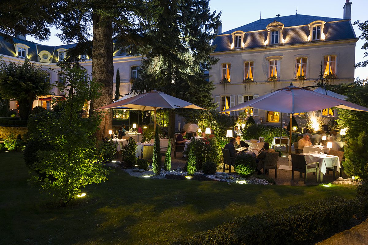 the outside of a white hotel with tables and parasols in a garden