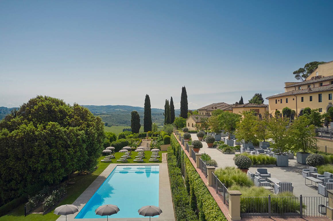 A swimming pool surrounded by a hotel trees and hills and fields