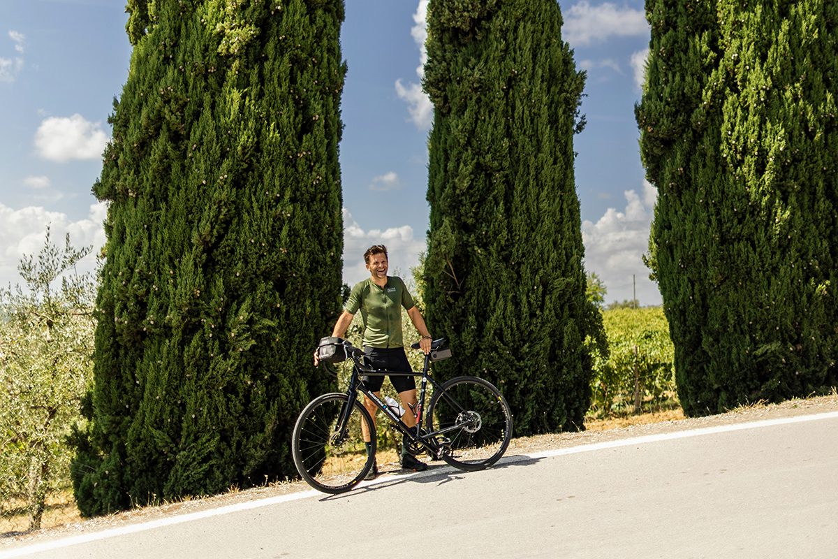 Man standing next to his bike by a sunny slanted road