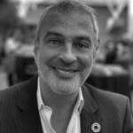 A man smiling wearing a white shirt and grey jacket