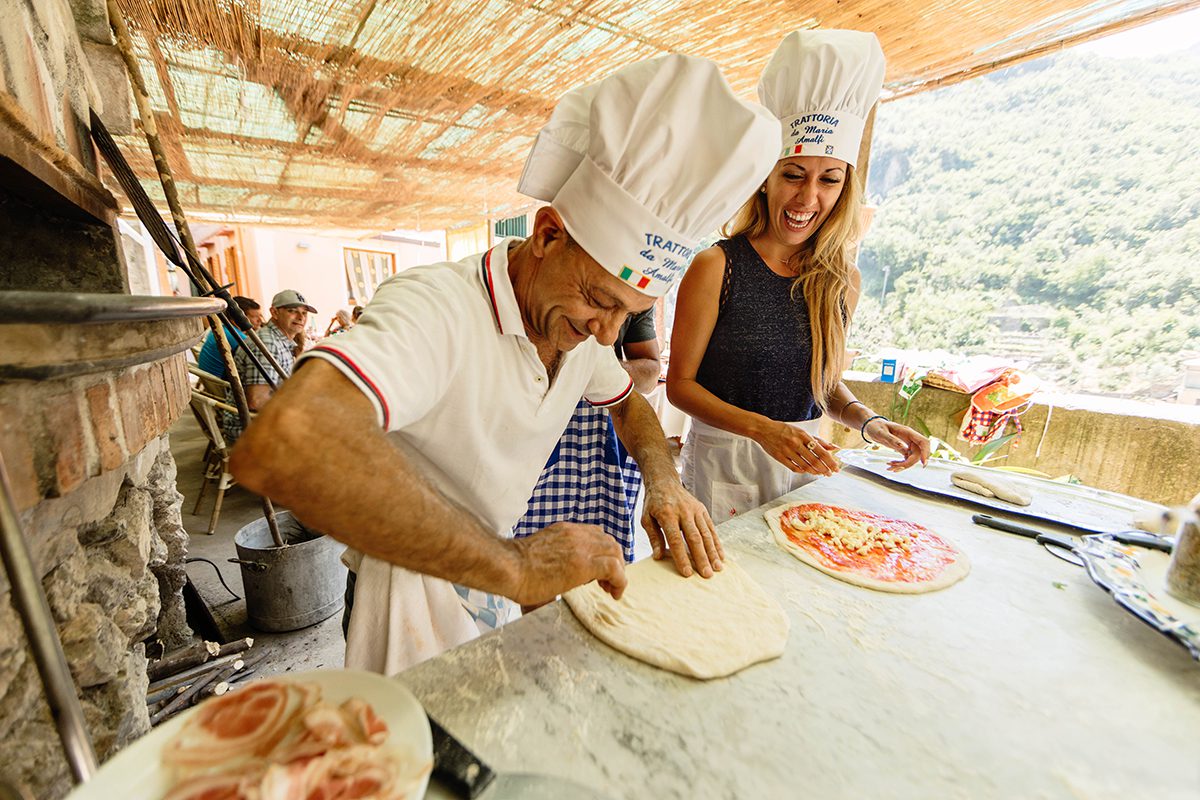 Two chefs cooking pizzas in brightly lit restaurant