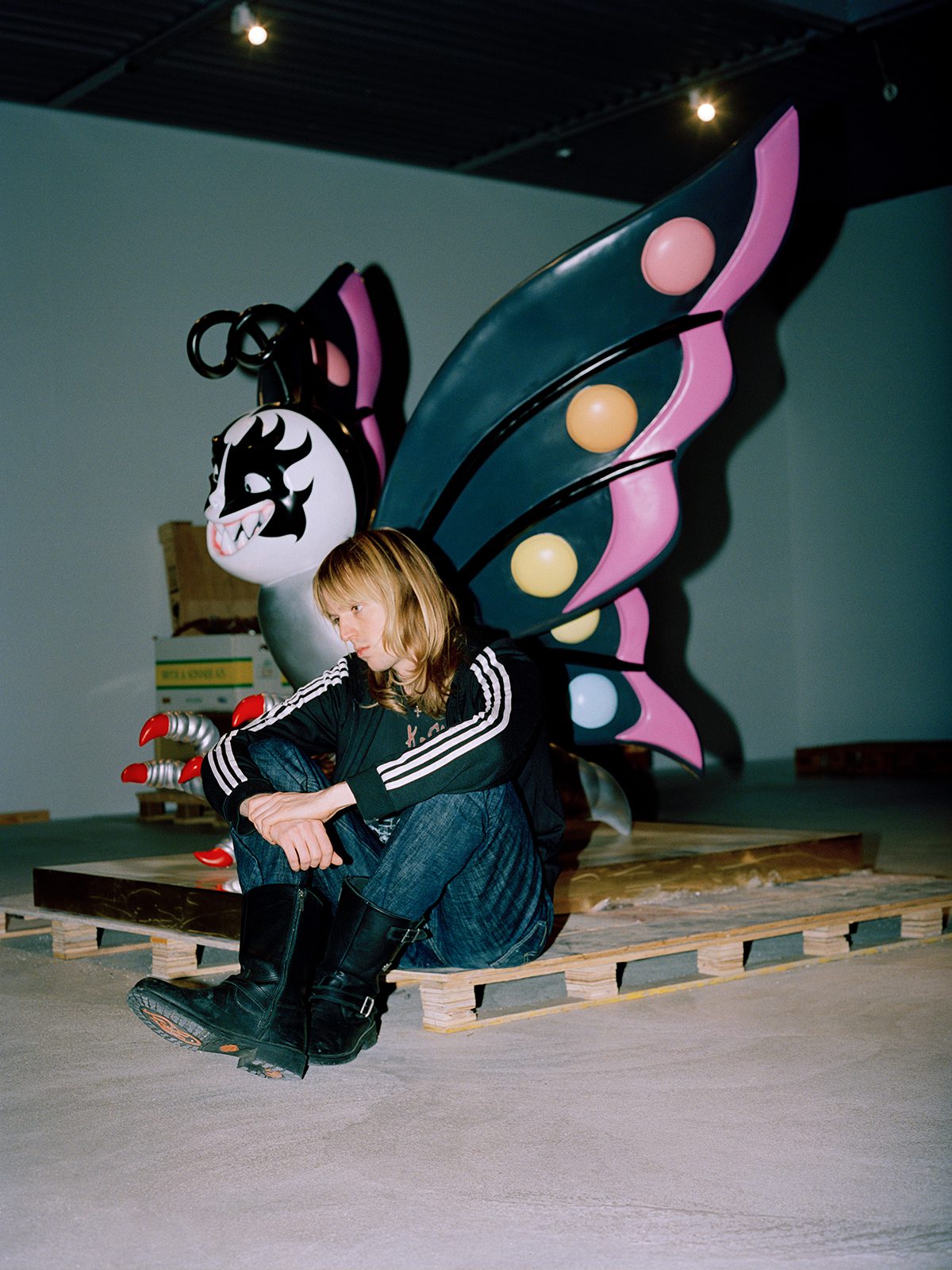 A person sitting on the floor wearing jeans and a black and white striped hoodie sitting next to a butterfly structure