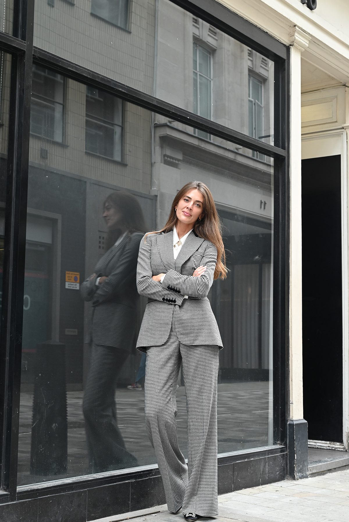 A girl standing in front of a large window wearing a grey striped suit