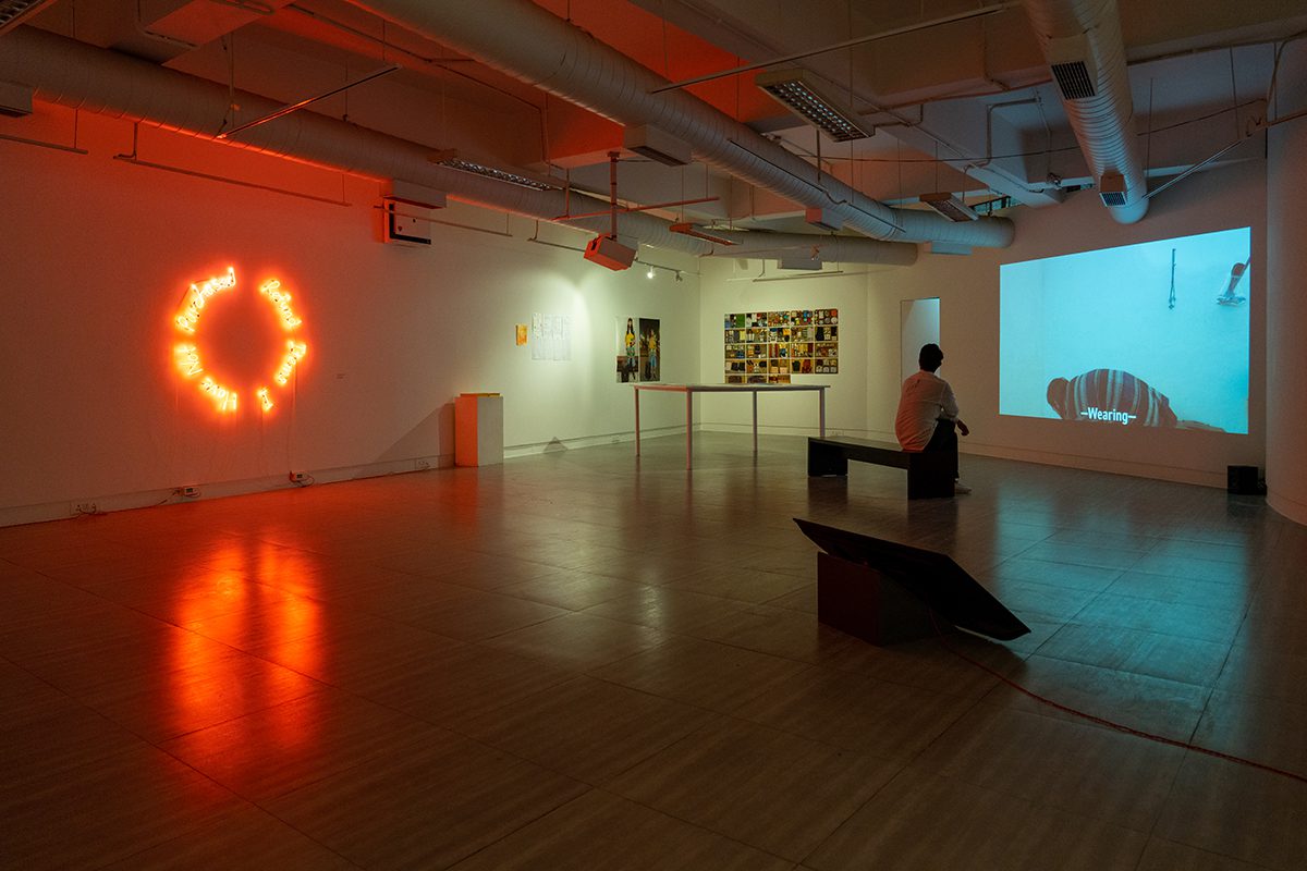 A room with art and a red light a man sitting on a bench watching a video from a projector