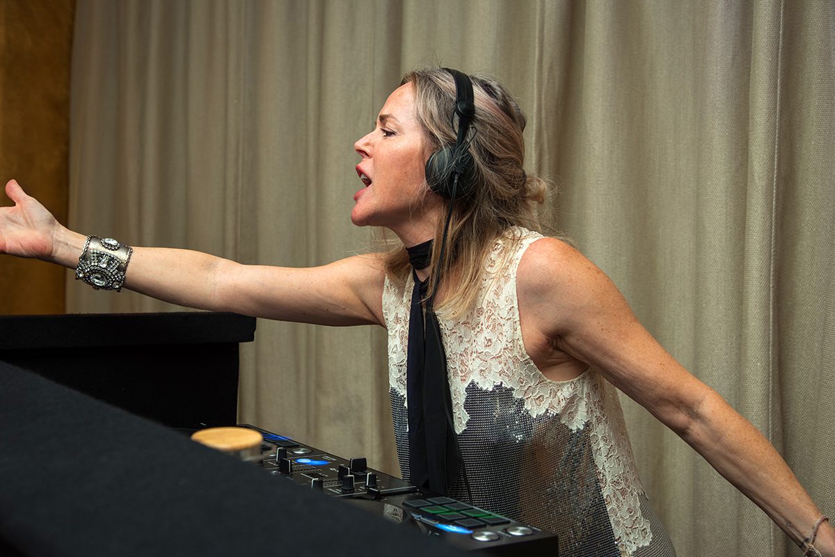 A woman DJ behind decks dancing with headphones on