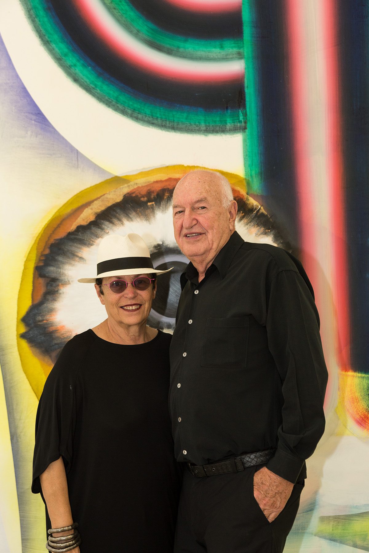 A man and woman wearing black standing in front of a colourful painting
