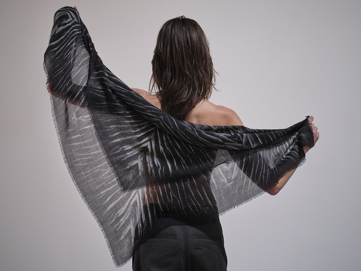A woman holding a black and grey feather print scarf around her back
