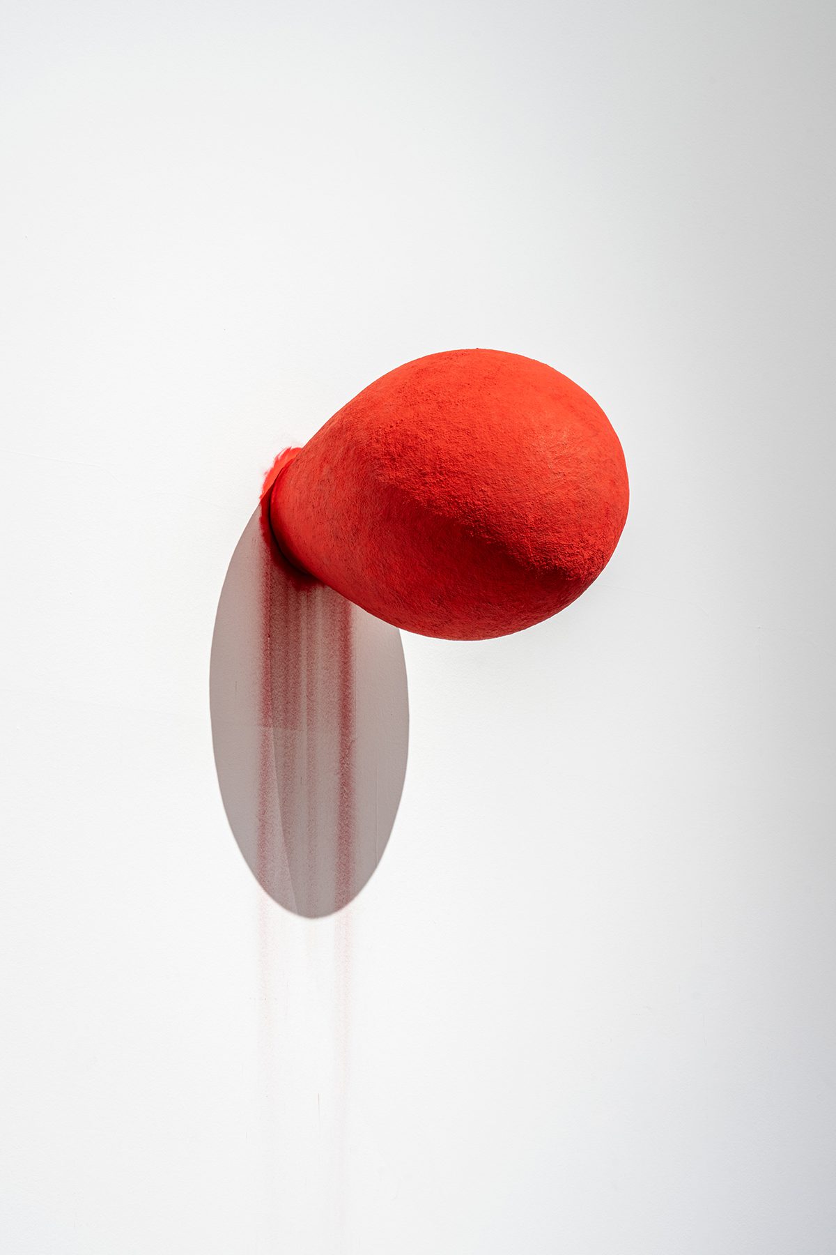 A red ball of paint on a white wall with red paint dripping 