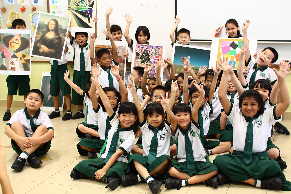 children in green and white uniform sitting on the floor with their hands in the air