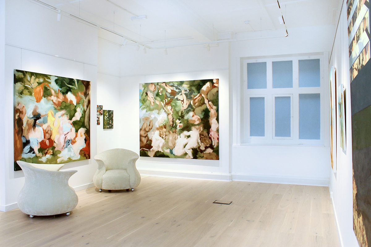 Green and pink paintings on white walls with white seats in the room on the wooden flloor