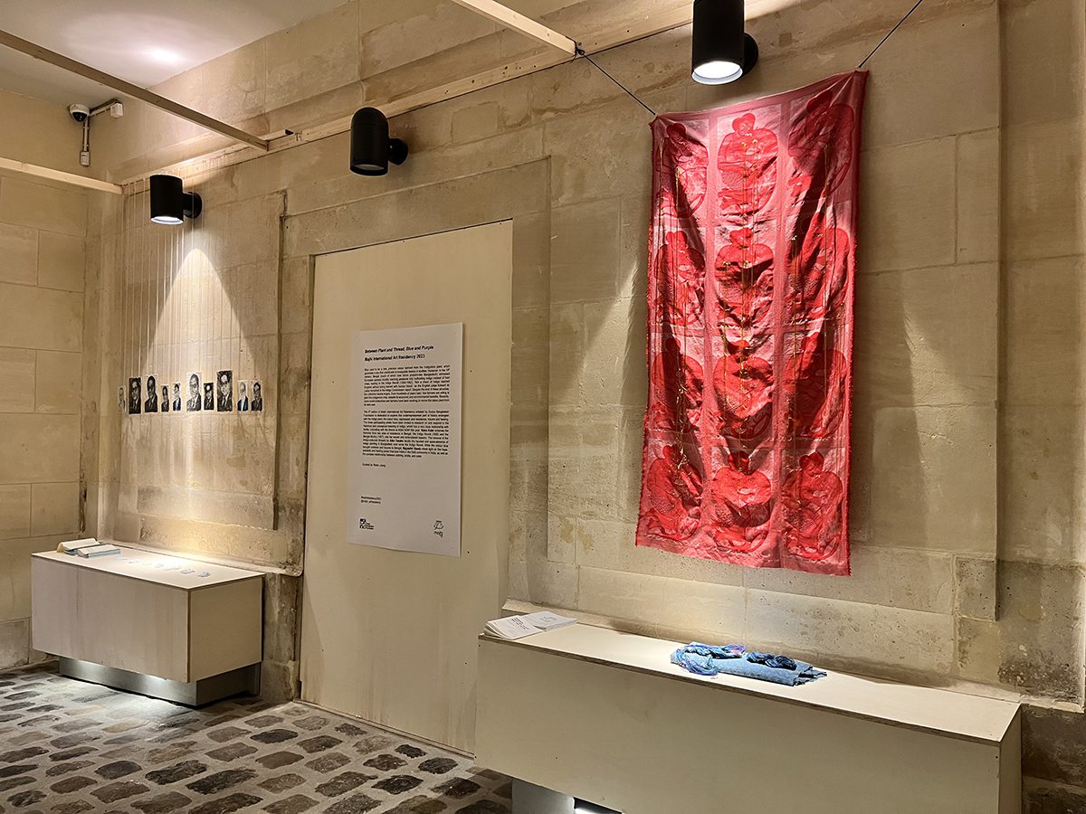 A room with a red tapestry hanging on the all and pictures hanging on strings beside