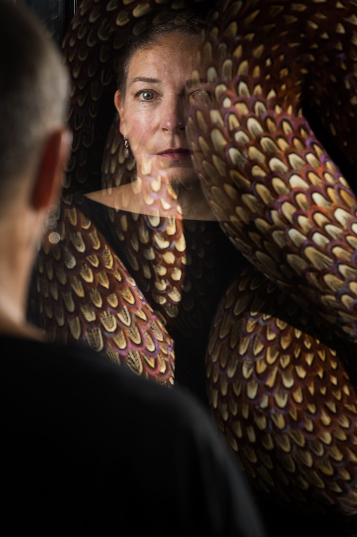 A woman's reflection by a feather sculpture