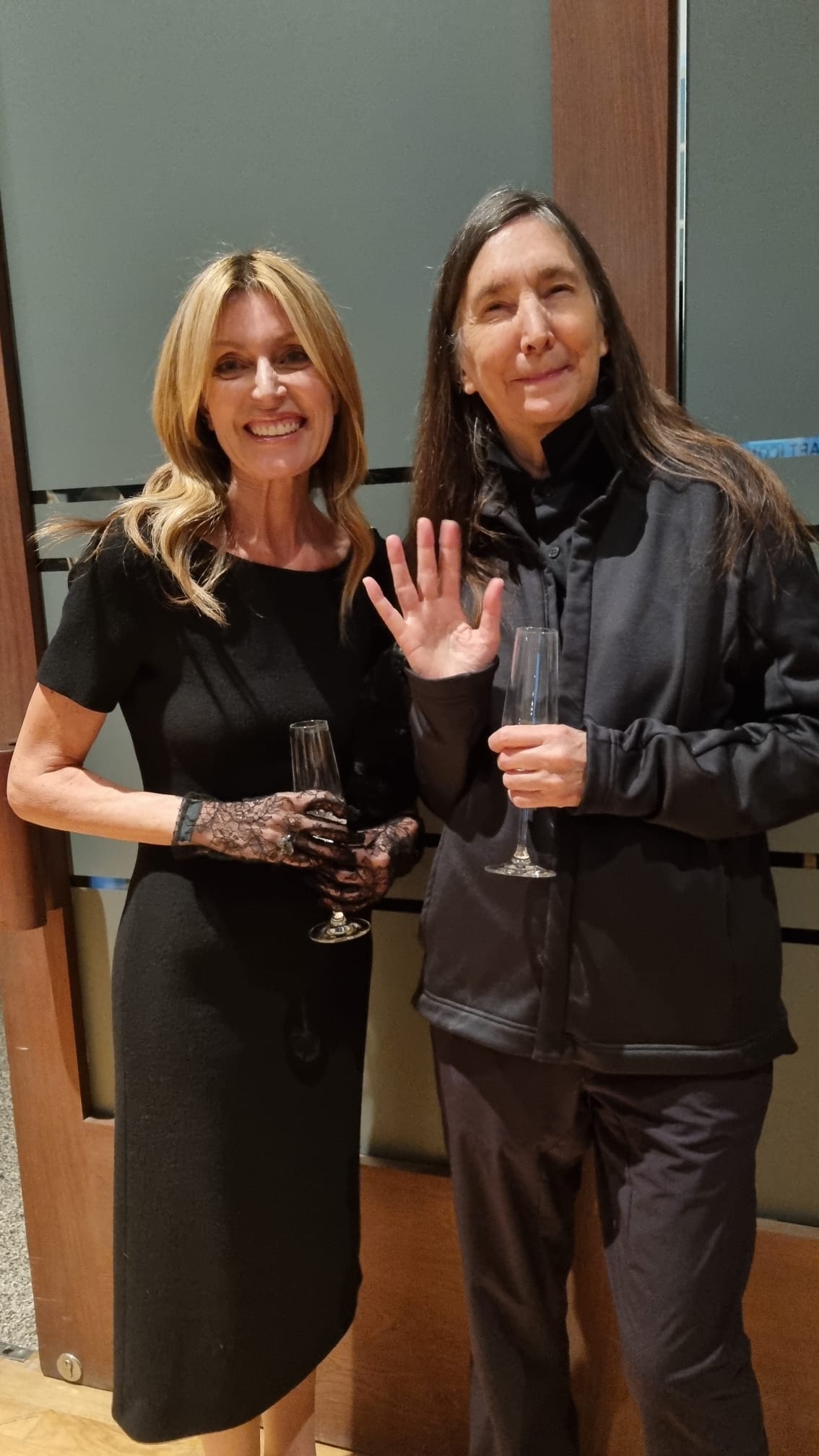Two women standing together, one waving her hand