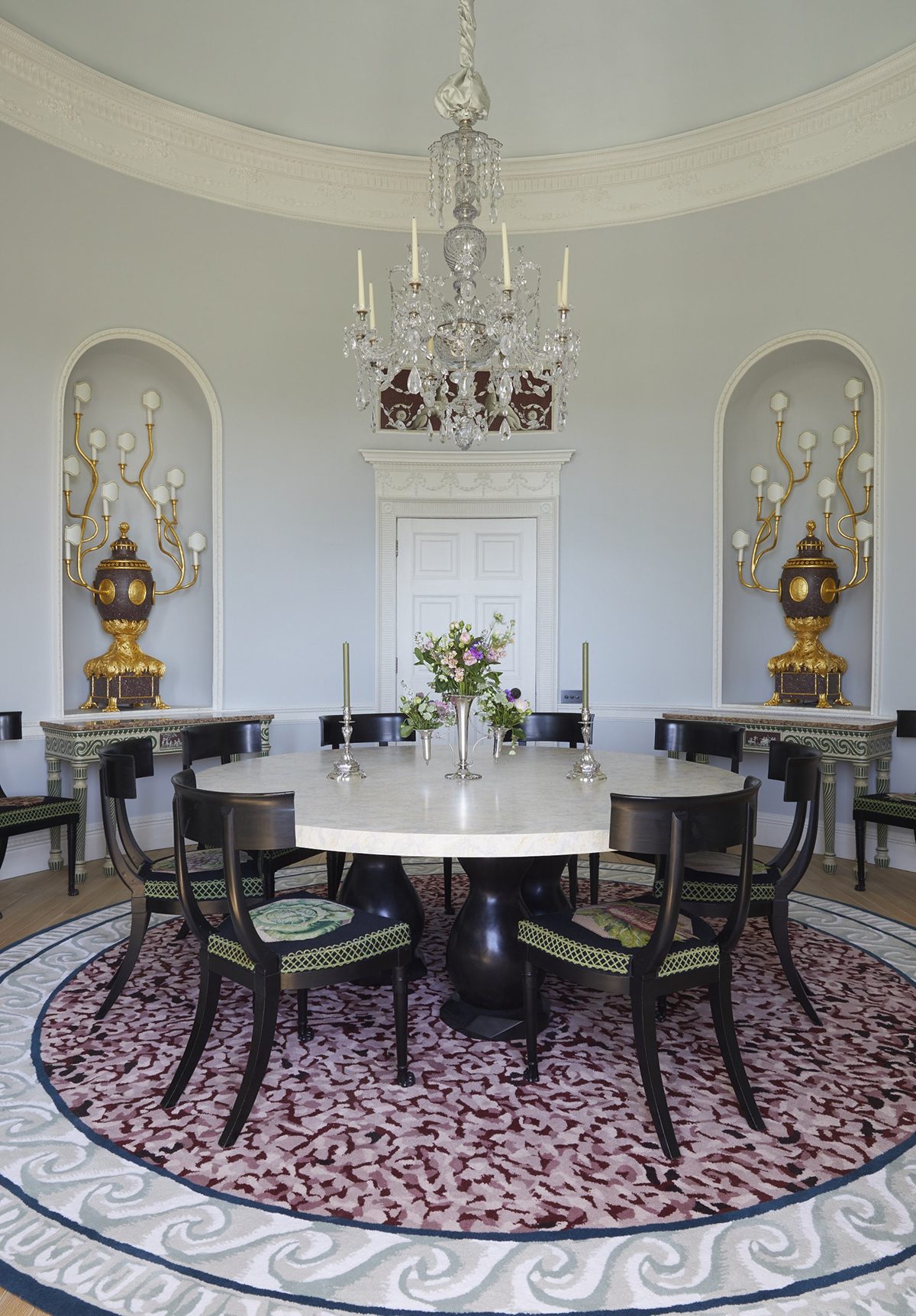 A dining room with a round table and green and wooden chairs with a purple patterned carpet
