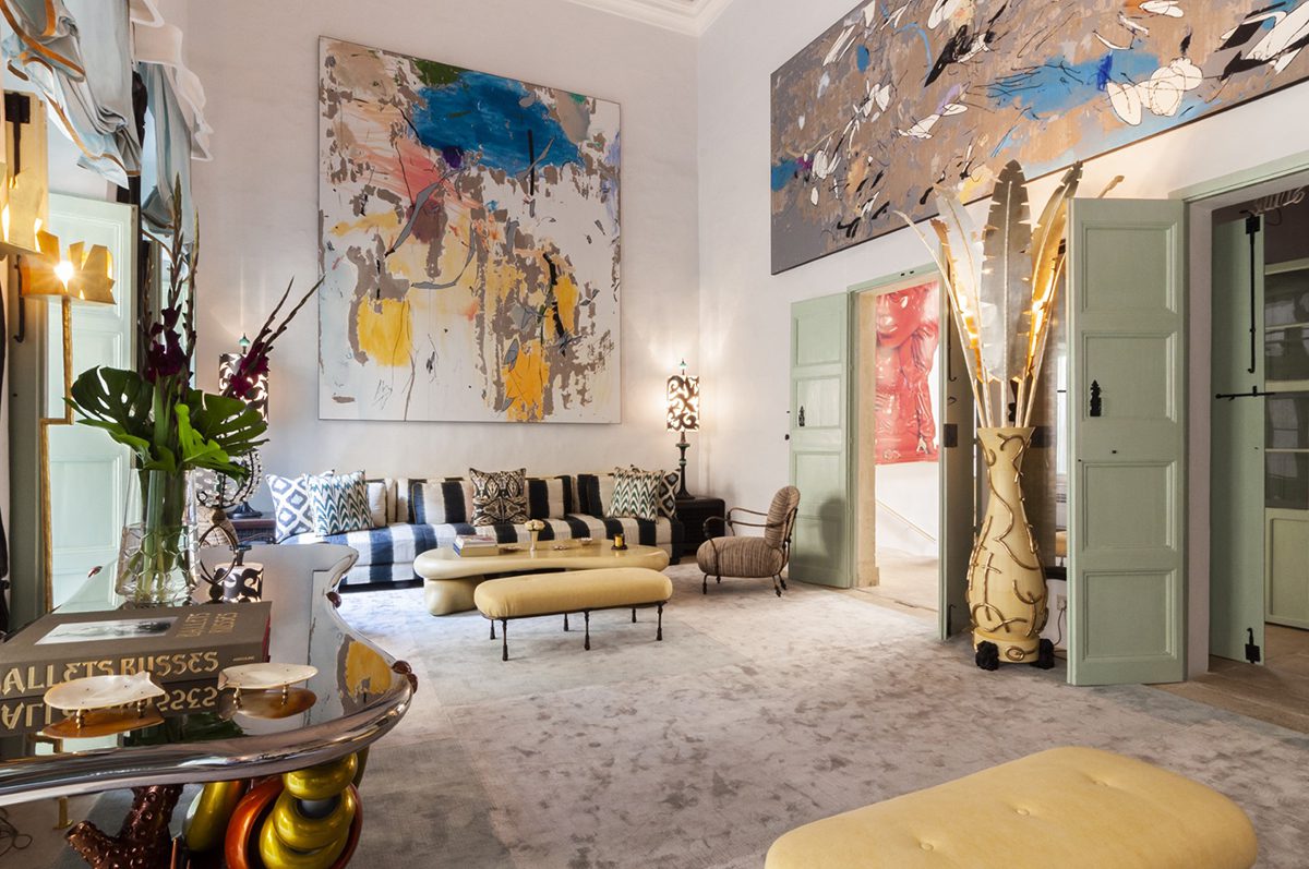 A room with a large colourful painting behind a striped blue couch with touches of gold around the room