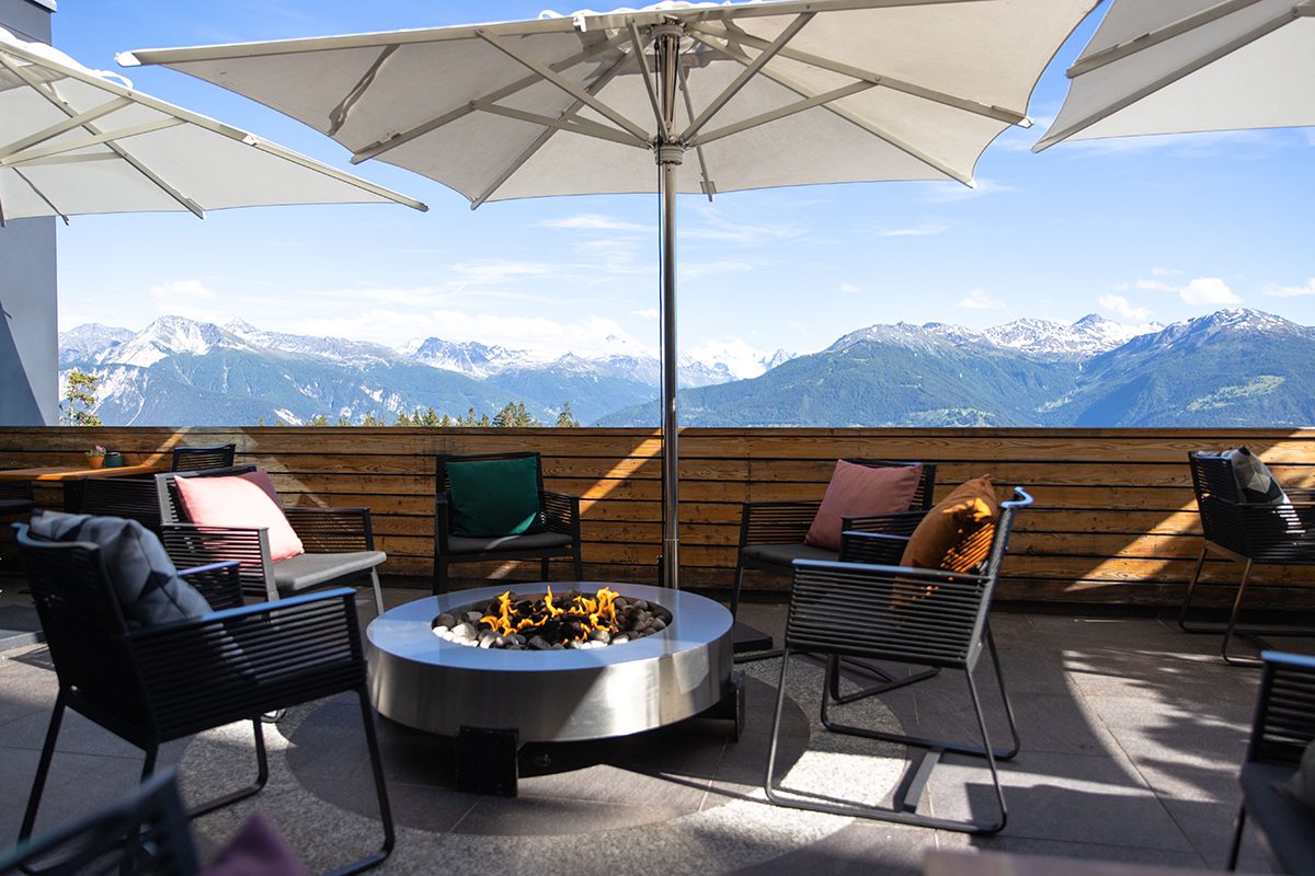  A terrace with a fire pit in the middle surrounded by chairs with cushions and a parasol