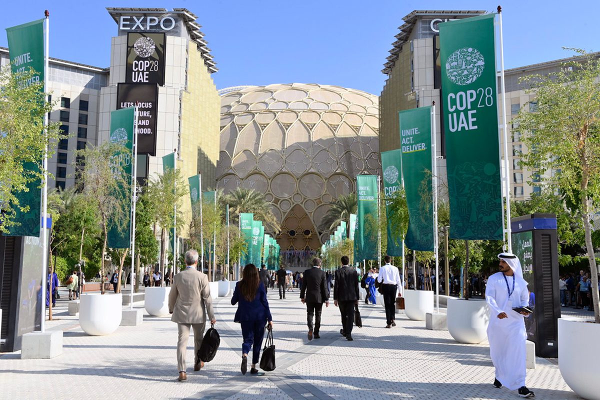 People walking in and out of a building that has signs to COP28