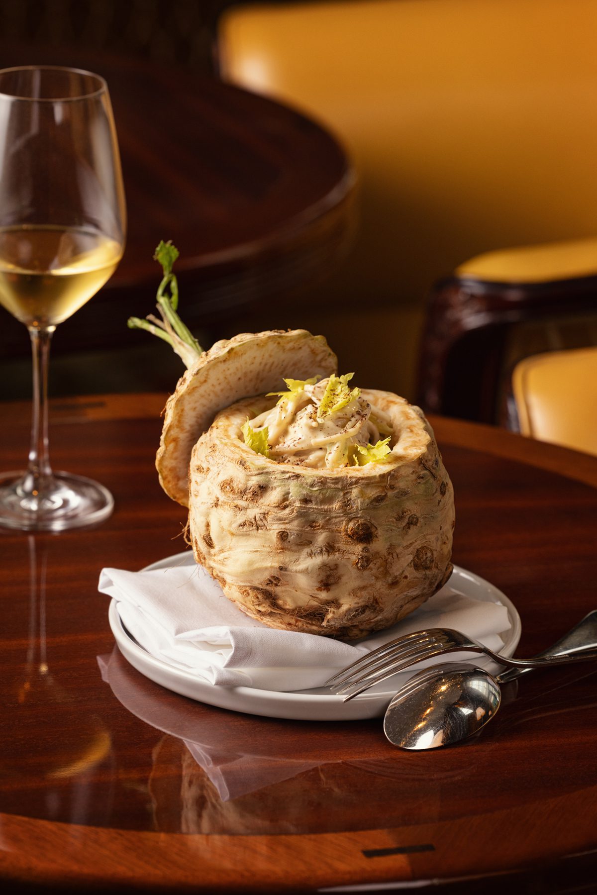 A vegetable opened up with food inside it on a plate next to a glass of wine on a wooden table