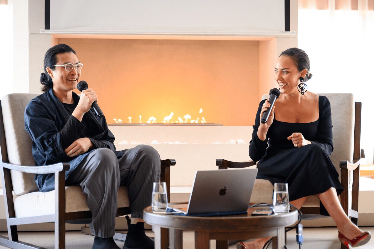 A man and woman sitting by a table with a laptop speaking into microphones