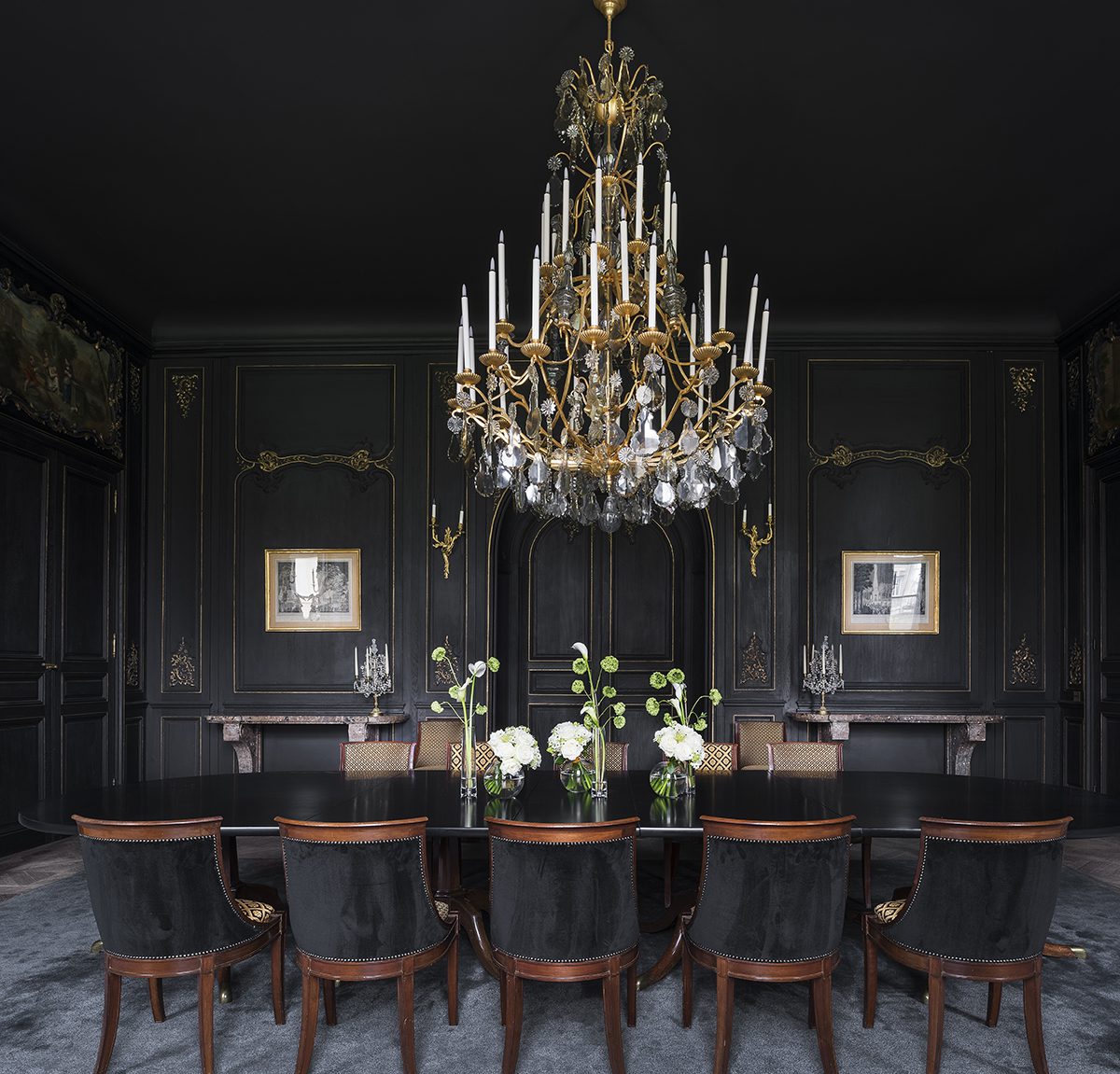 A dark dining room with a chandelier hanging over the table
