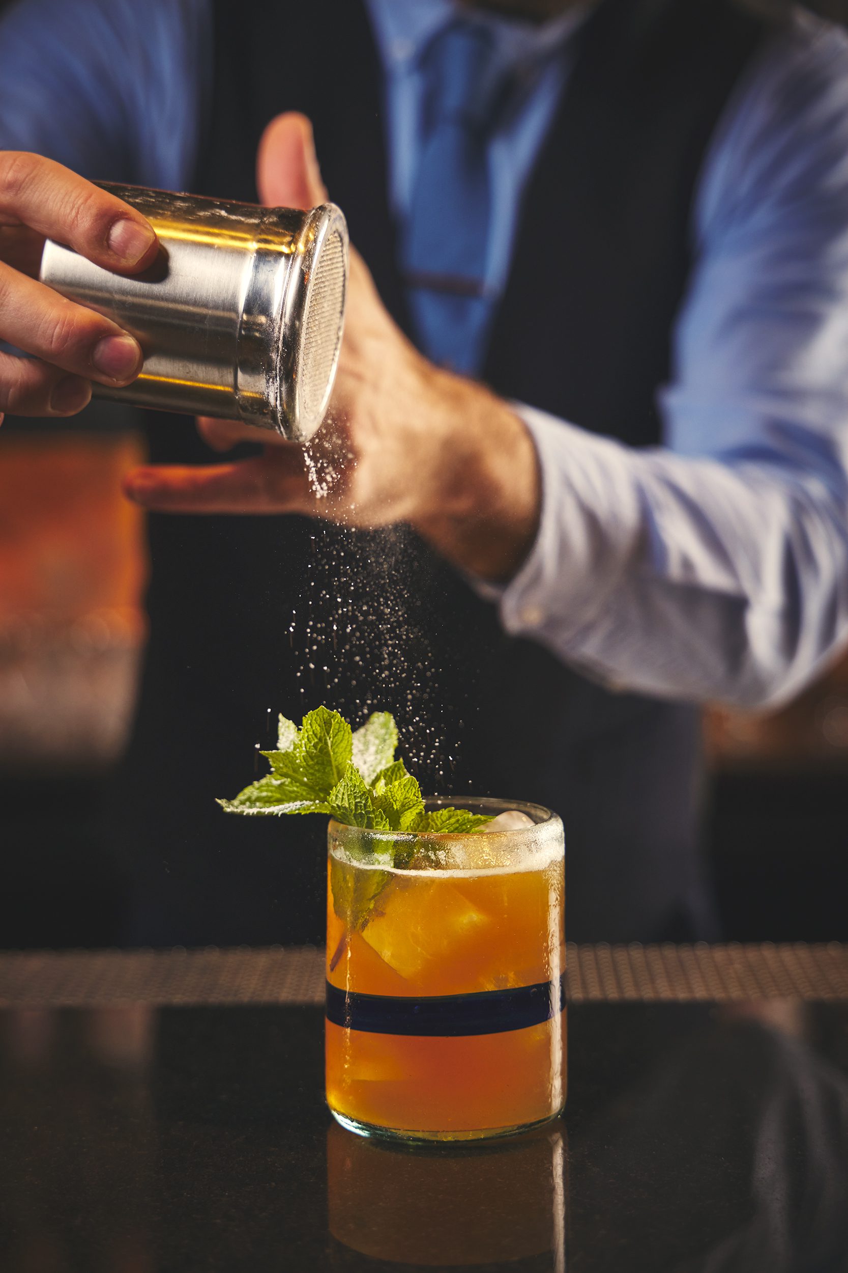 cocktail with a mint leaf and a man pouring sugar over it