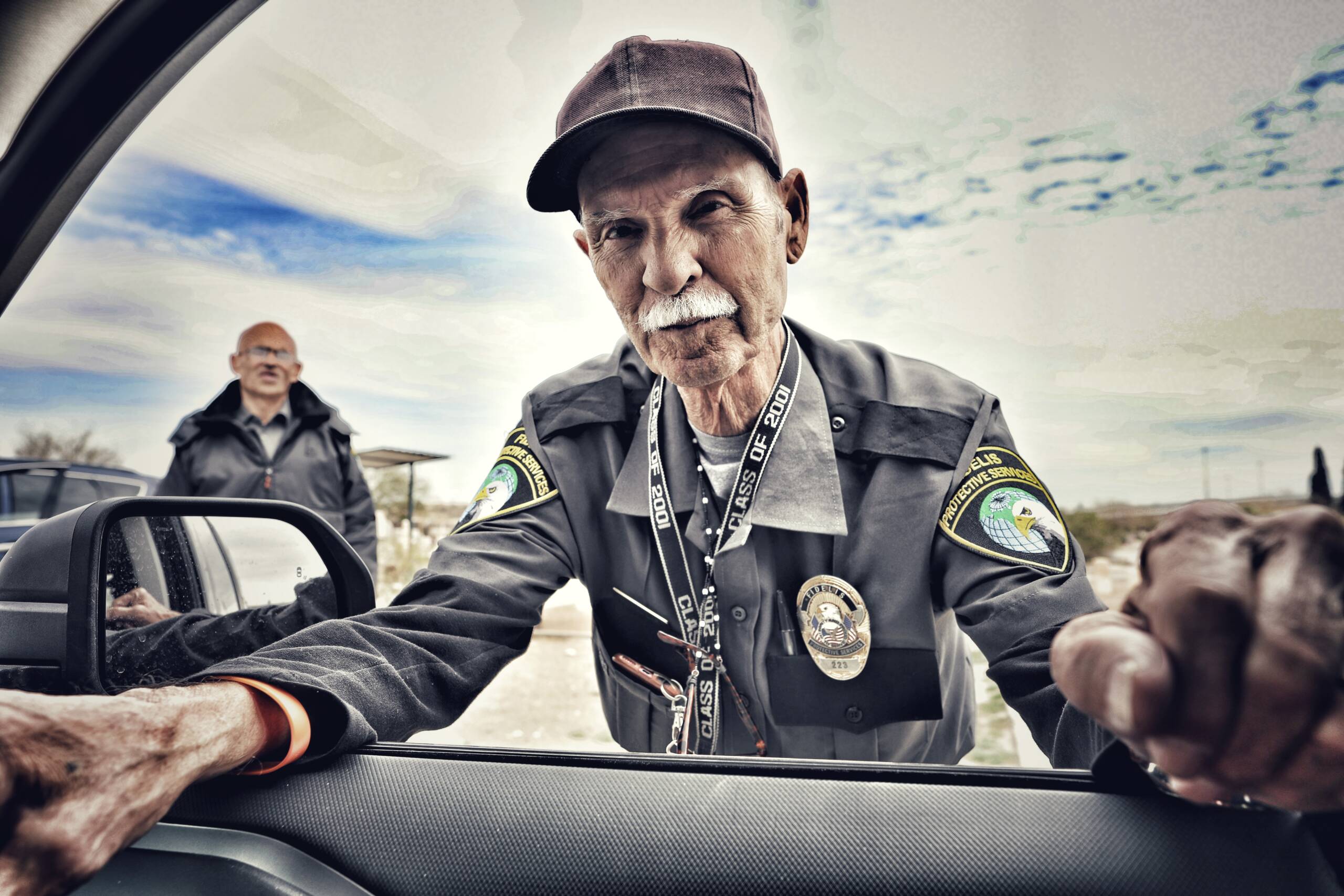A policeman leaning into a car with a man behind, and a big sky
